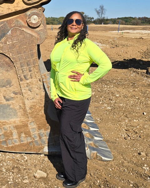 Tammy Ristow, Owner, President, and CEO of Rams Contracting, standing beside a Rams excavator