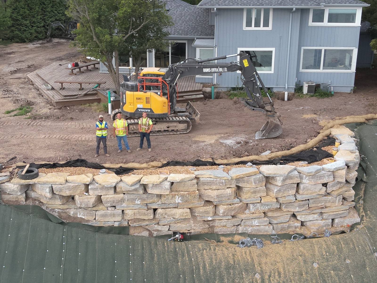 Rams crew standing beside a Rams excavator above a newly built limestone retaining wall
