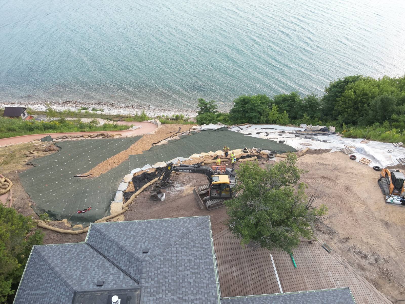 Aerial view of a Rams excavator stabilizing a lakefront bluff with erosion matting and stone