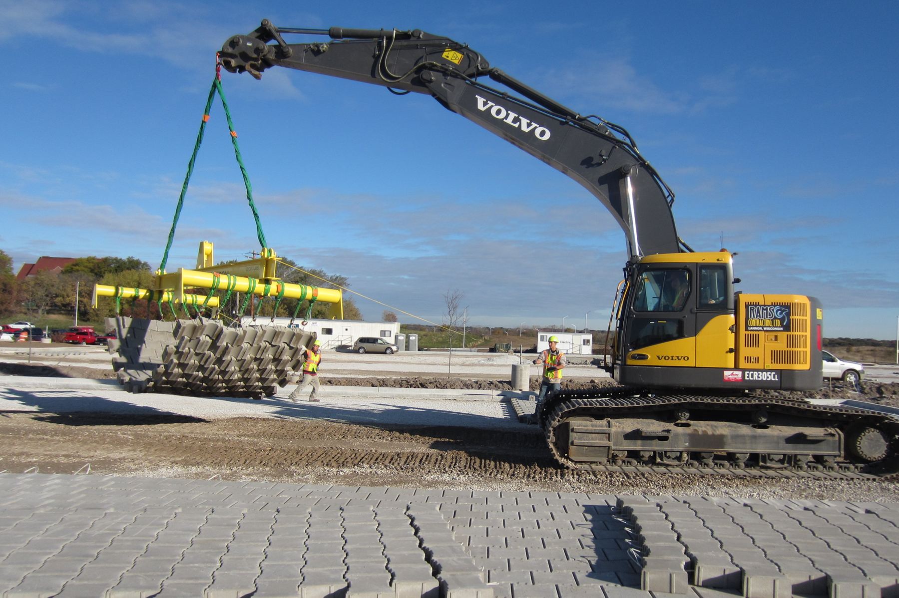 Volvo excavator lifting paver bundles under a blue sky